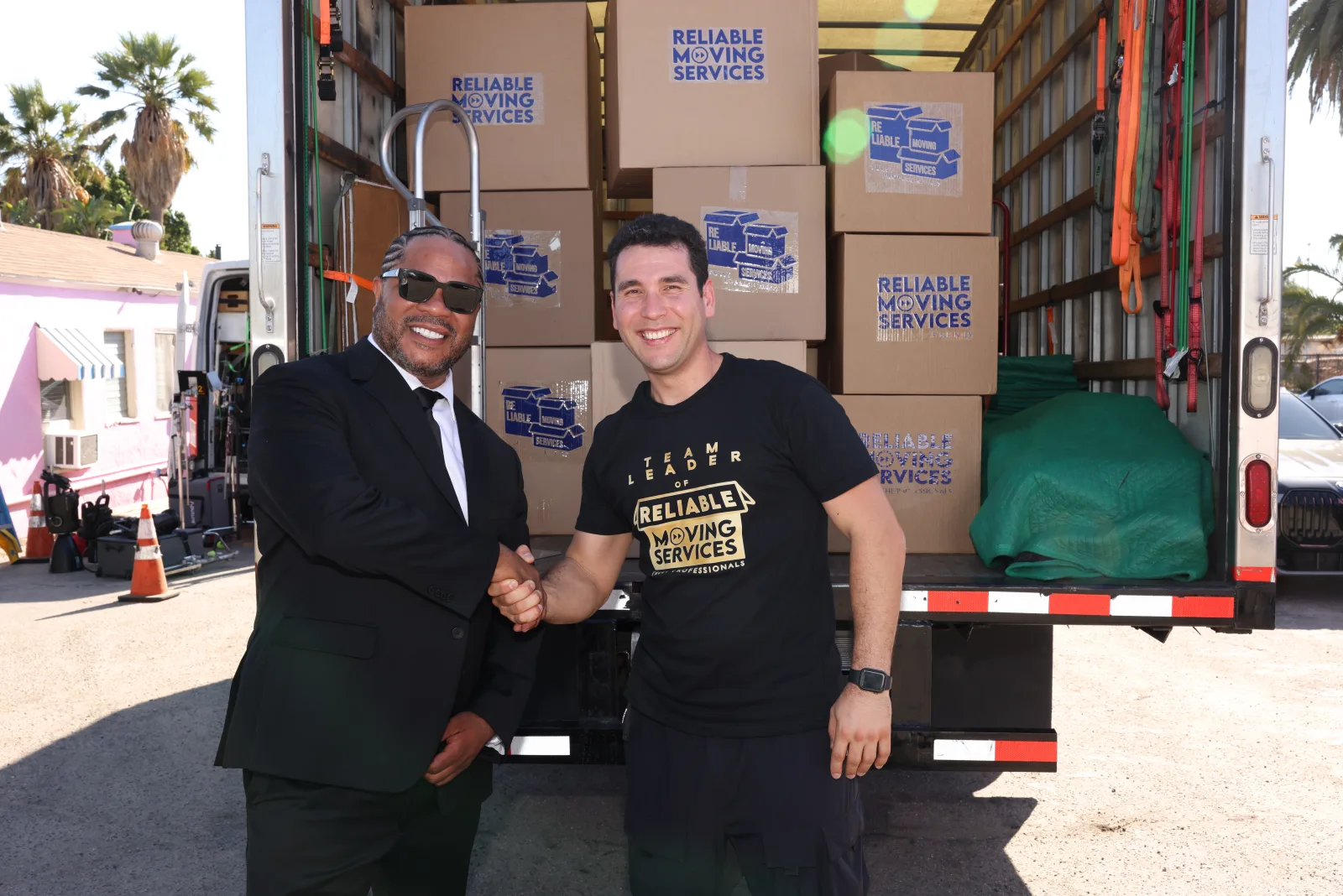 Reliable Moving Services team leader shaking hands with a customer by a truck of branded boxes in Orange County